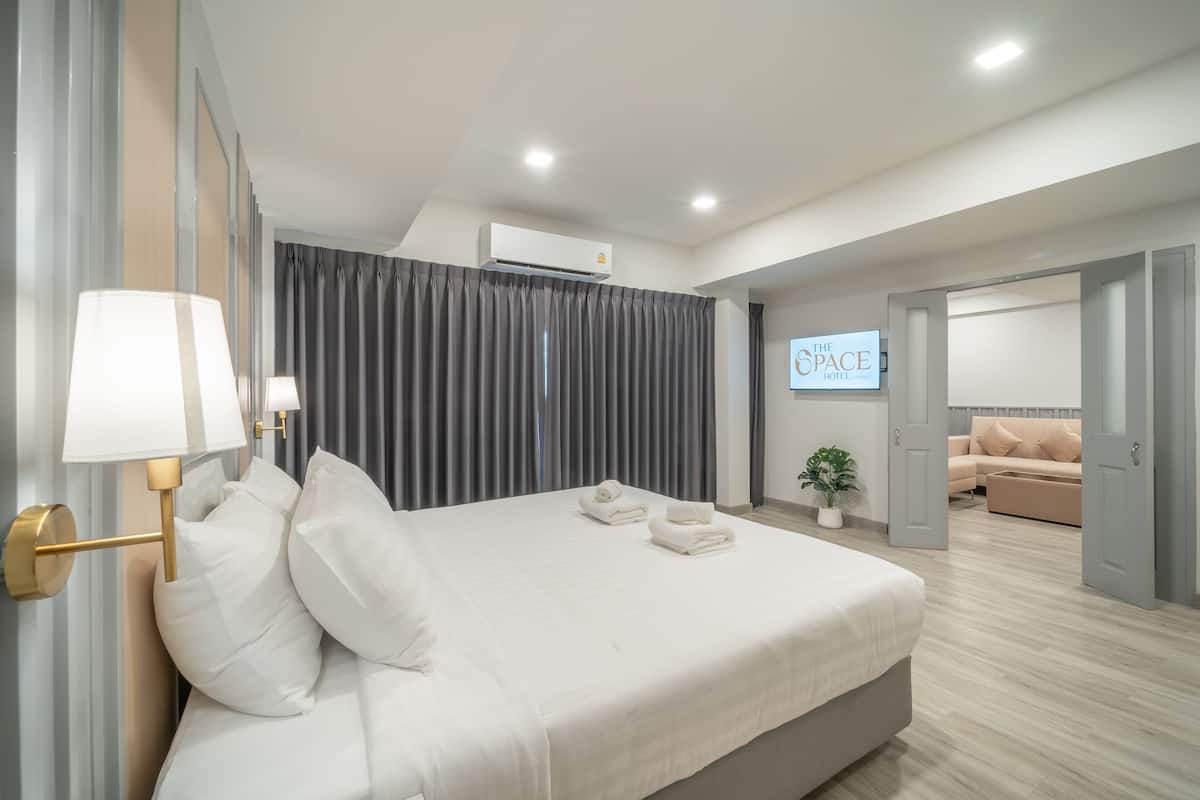 Une chambre d’hôtel moderne avec un grand lit, un téléviseur à écran plat, un canapé et une plante en pot.