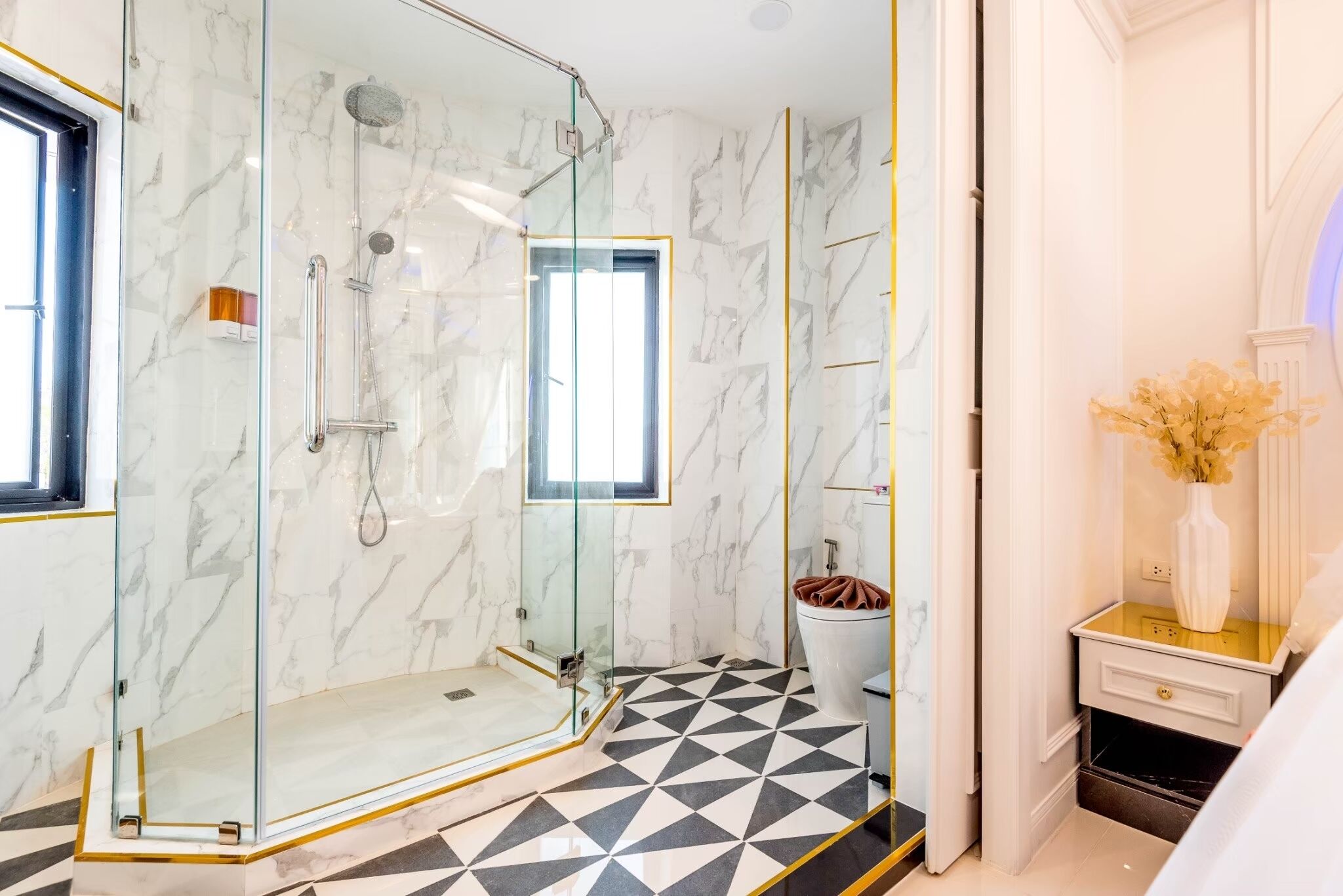 A modern bathroom with a glass-enclosed shower, marble walls, and a geometric black and white tile floor.