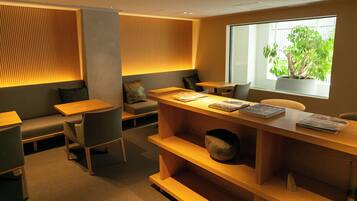 A modern, well-lit room with a wooden reception desk, seating area, and a large window with a view of greenery.