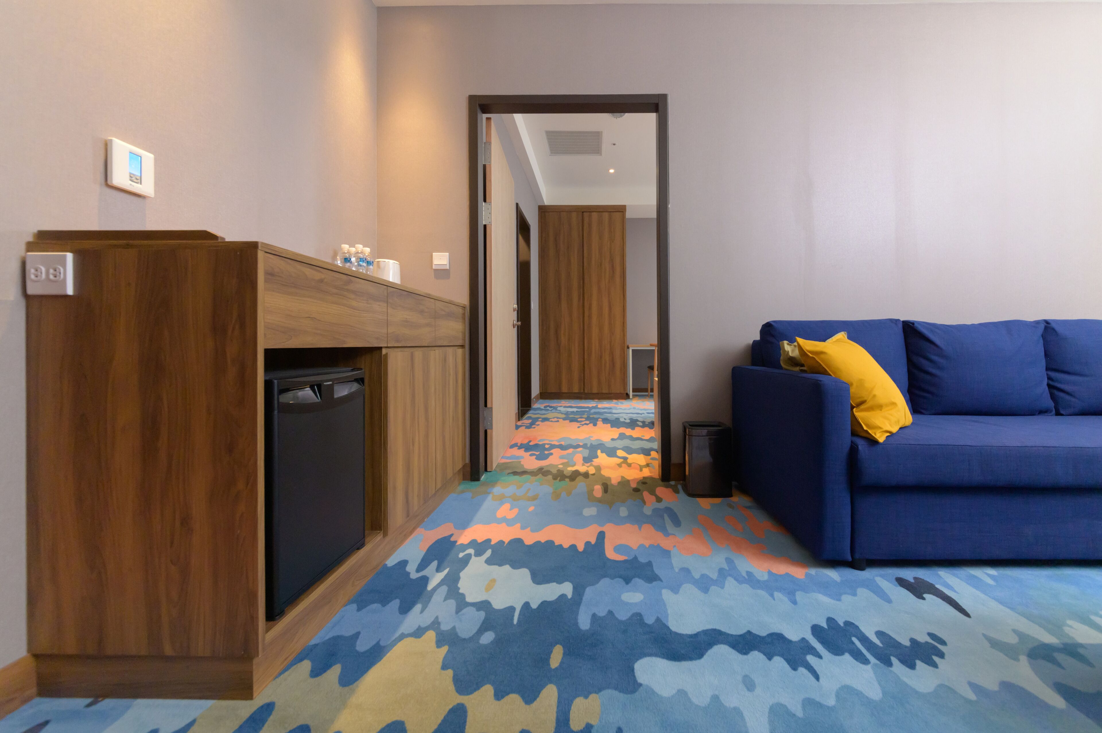 A hotel room with a blue sofa, a wooden cabinet, and a colorful carpet.
