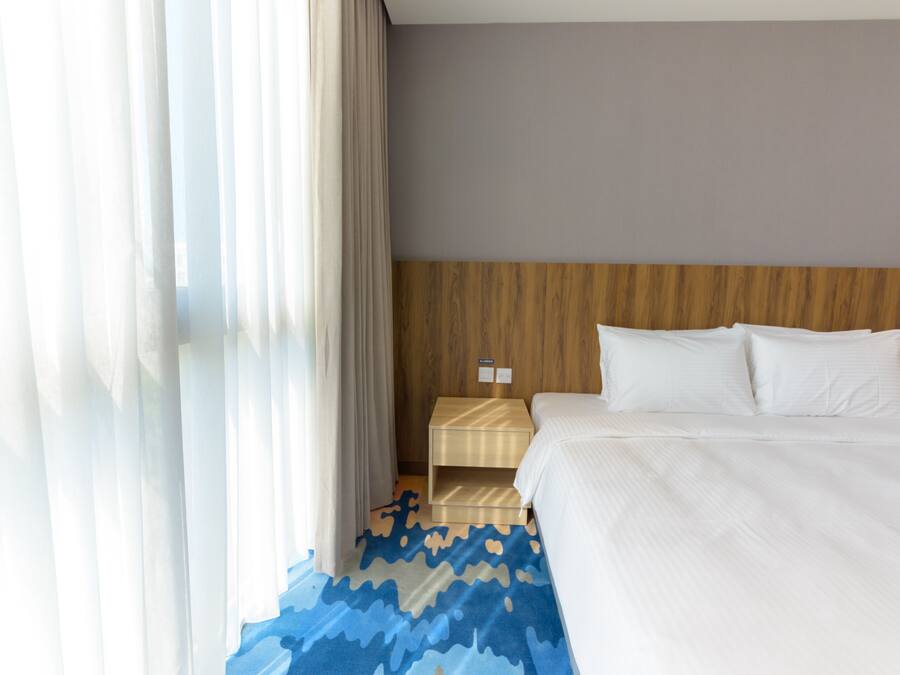 Ein Hotelzimmer mit einem hölzernen Kopfteil, einem Bett mit weißer Bettwäsche, einem Nachttisch mit einer Lampe und einem gemusterten Teppich.