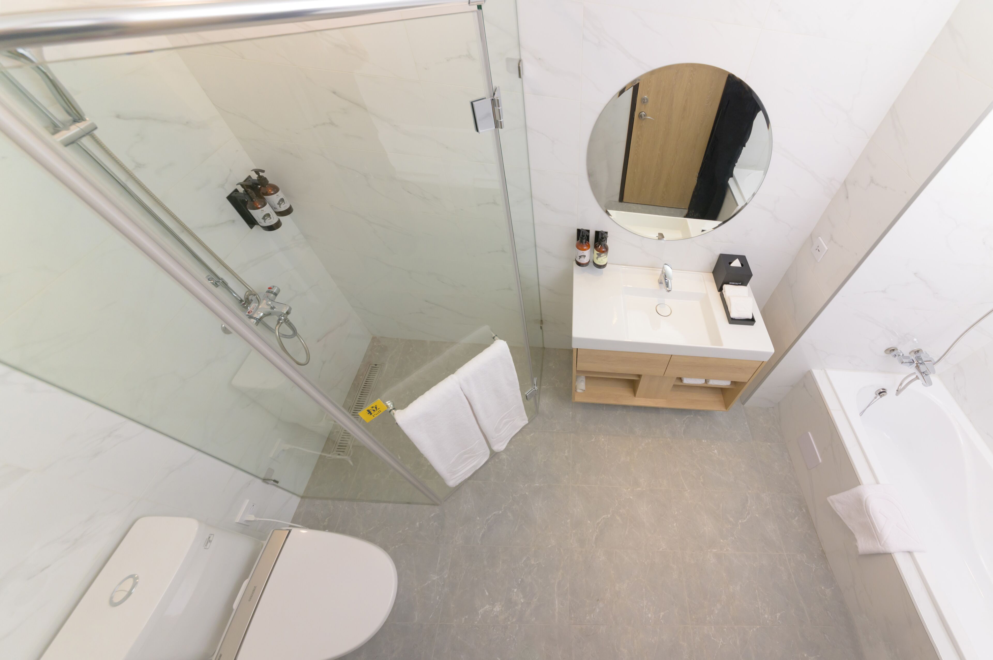 Un baño moderno con cabina de ducha de vidrio, un espejo redondo, un lavabo con tocador de madera y una bañera.