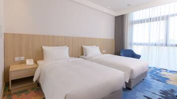 A hotel room with two beds, a nightstand with a phone, a blue armchair, and a large window with curtains.