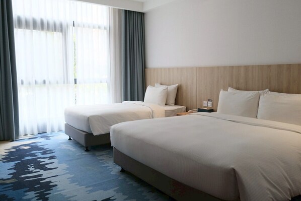 Ein Hotelzimmer mit zwei Betten, einem großen Fenster mit Vorhängen, einem hölzernen Kopfteil und einem gemusterten Teppich.