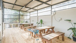 A covered outdoor area with wooden picnic tables and benches, potted plants, and a view of the surrounding greenery. - Today Seogwipo (Seogwipo)
