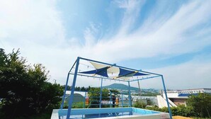 A swimming pool with a blue frame and a shaded area, surrounded by greenery and buildings in the background. - Today Seogwipo (Seogwipo)