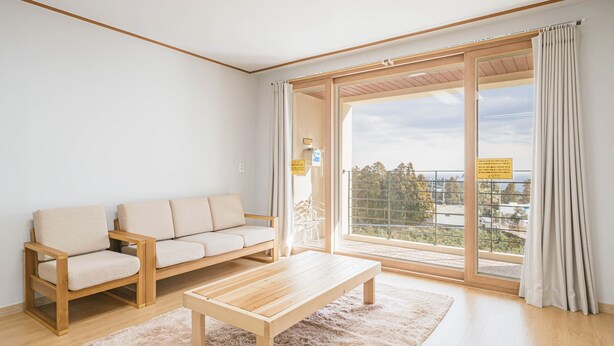 A modern living room with a sofa, a wooden coffee table, and a large sliding glass door leading to a balcony. - Today Seogwipo (Seogwipo)