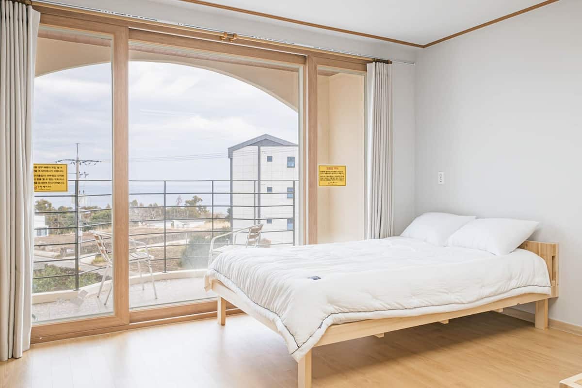 A bedroom with a bed, a large window, and a view of buildings outside.