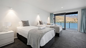 Una habitación de hotel moderna con una cama grande, una cama más pequeña, un escritorio y vistas a un lago y montañas.