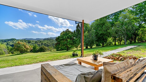 Eine Terrasse im Freien mit einer Holzbank, einem Tisch mit einer Topfpflanze und Blick auf eine grüne Landschaft mit Bäumen und Hügeln.