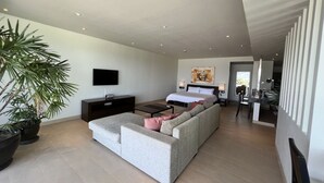 A modern living room with a grey sofa, a flat-screen TV, a large Buddha painting, and a dining area with a table and chairs. - Stunning Ocean View Studio Apartment (Tambon Rawai)
