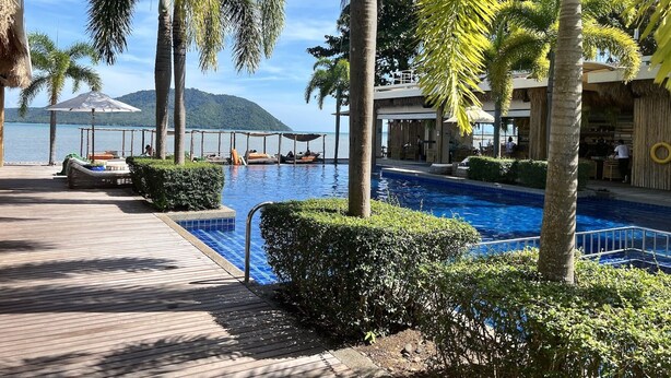 A pool area with a wooden deck, palm trees, and a view of the sea. - Stunning Ocean View Studio Apartment (Tambon Rawai)