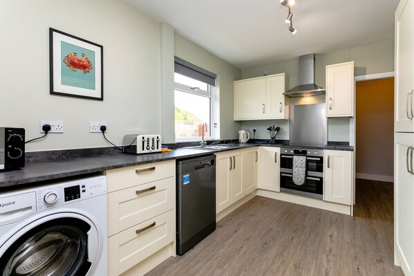 A modern kitchen with a washing machine, dishwasher, oven, and a large window.