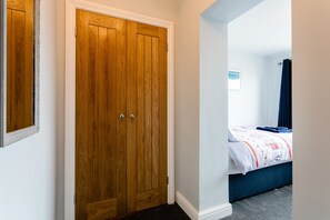 Un dormitorio con un armario de madera, una cama con cabecero azul y una ventana pequeña con vistas.