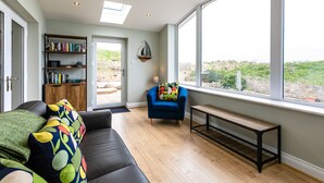 Un salon moderne avec un canapé en cuir noir, un banc en bois, un fauteuil bleu et une bibliothèque.