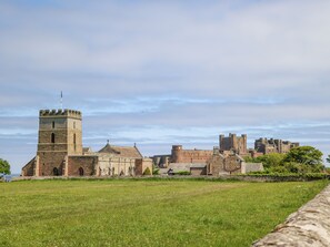 Un castillo histórico con una torre destacada, rodeado por un campo cubierto de hierba y un muro de piedra.