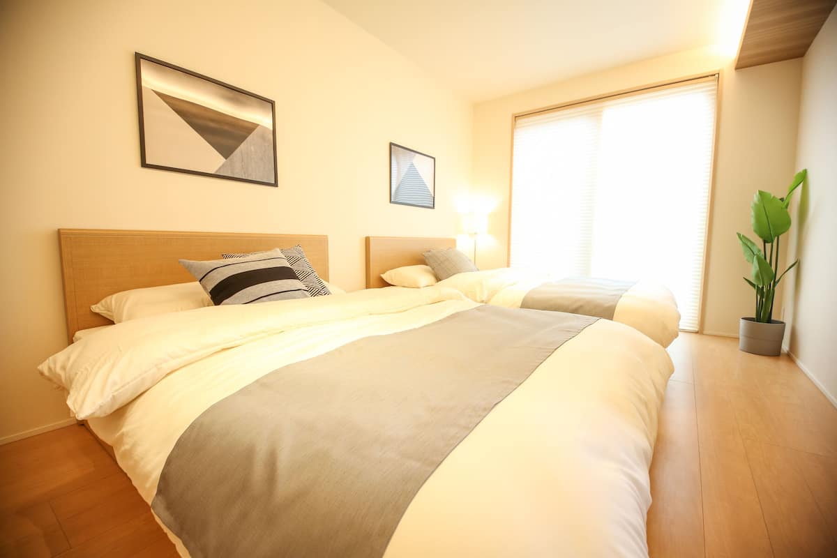Una habitación de hotel con dos camas, un ventanal grande y una planta en maceta.
