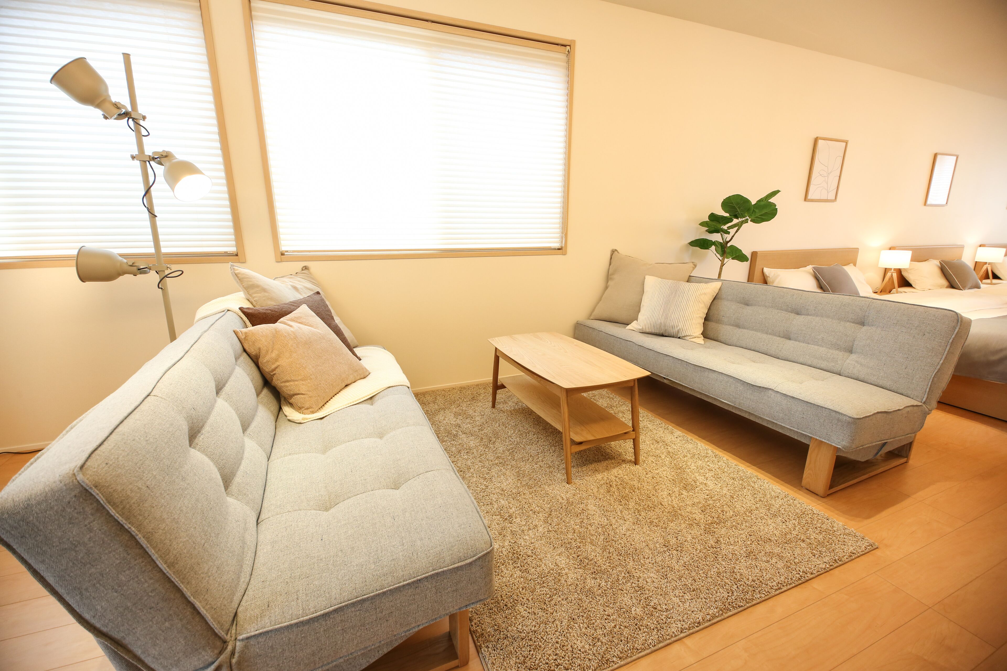 A modern living room with a grey sofa, a wooden coffee table, and a large window with blinds.