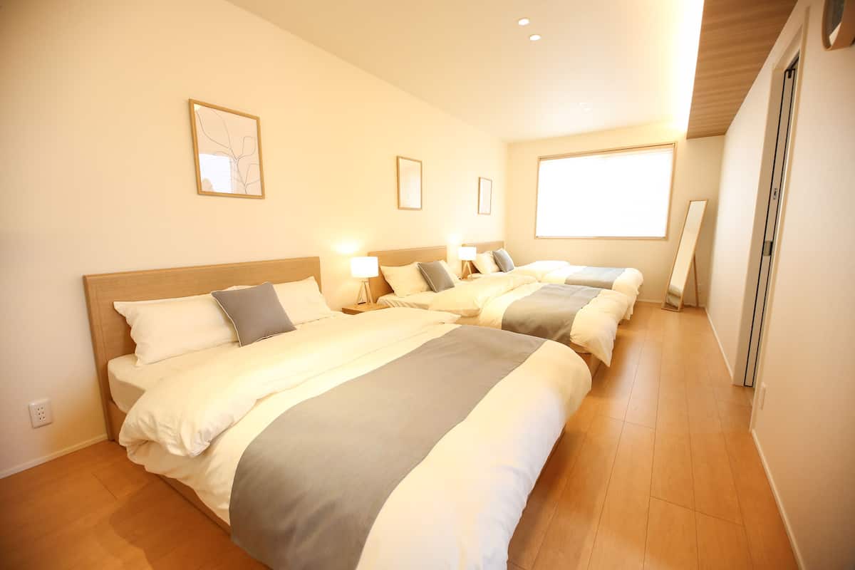 Habitación de hotel con tres camas, suelo de madera y un ventanal grande que proporciona luz natural.