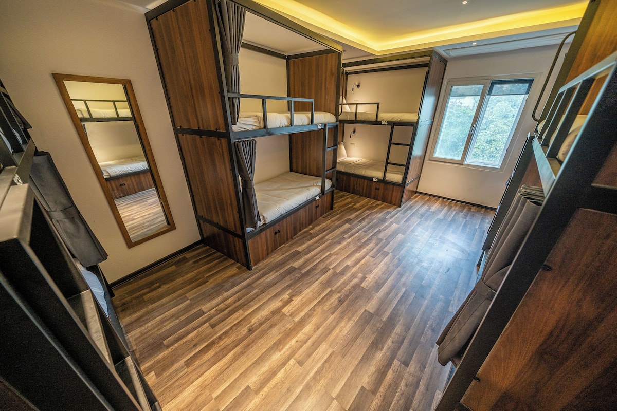A room with bunk beds, wooden flooring, a mirror, and a window.