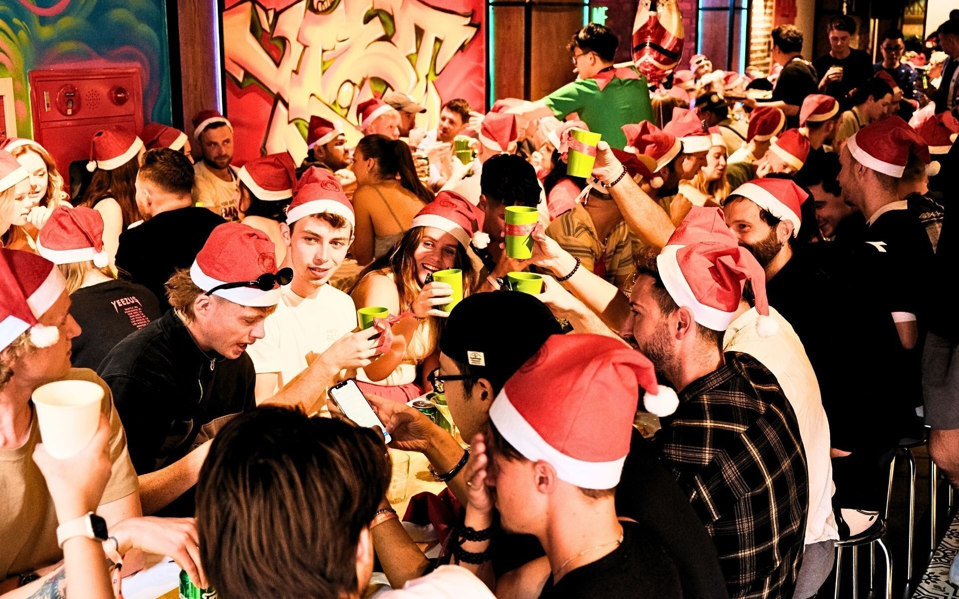 A crowded indoor event with people wearing Santa hats, suggesting a festive gathering.