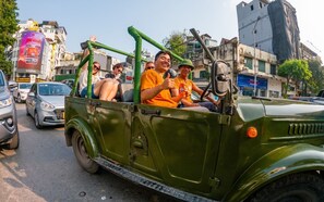 A green jeep with passengers, parked on a street with buildings and shops in the background. - Mad Monkey Hanoi - Hostel (Hanoi)