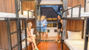 A dormitory room with bunk beds, a wooden interior, and a view of a building outside. - Mad Monkey Hanoi - Hostel (Hanoi)