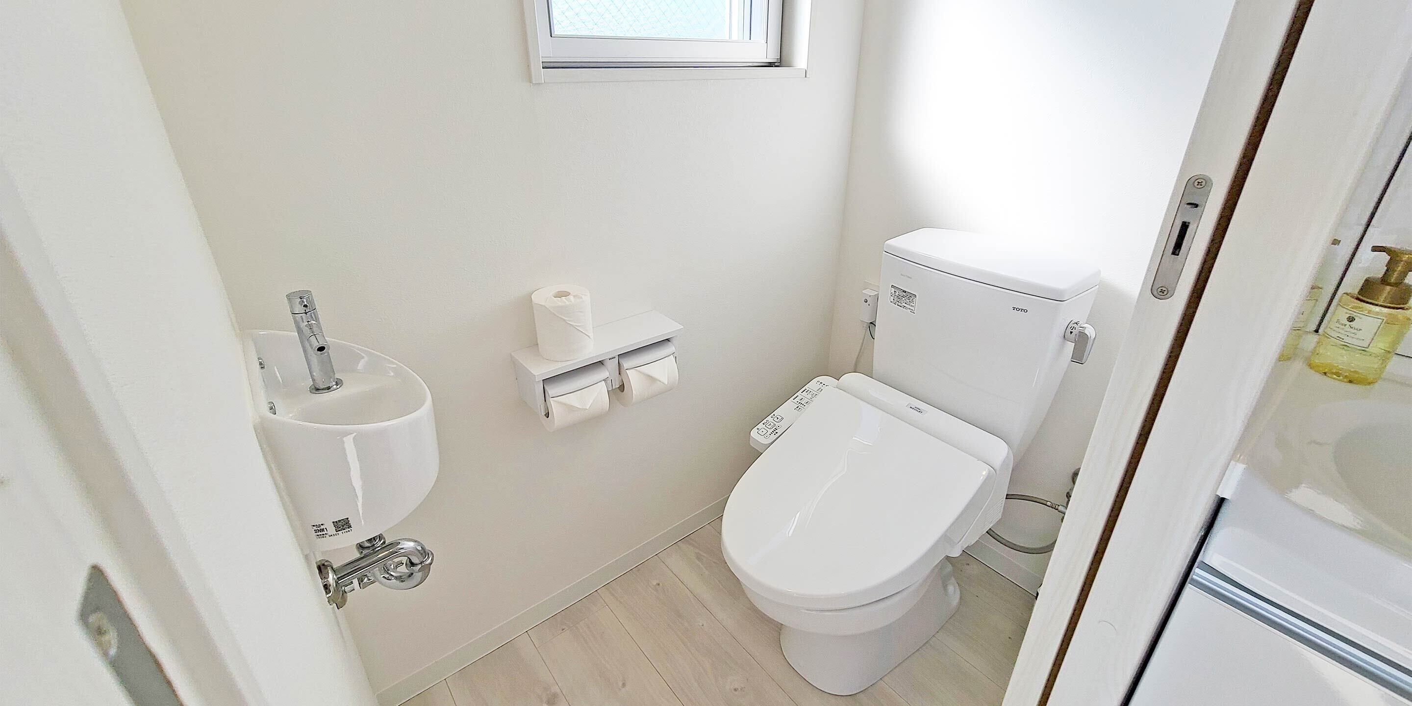 A small, clean bathroom with a toilet, sink, and a toilet paper holder on the wall.