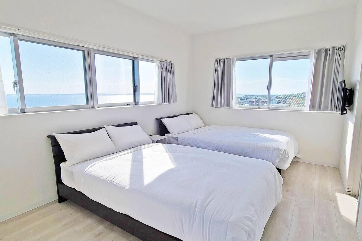 A bedroom with two beds, large windows, and a view of the sea.