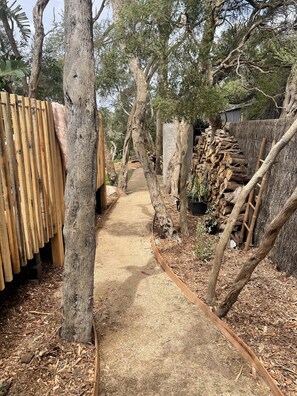 Walk along the winding pathway surrounded by trees and wooden structures.