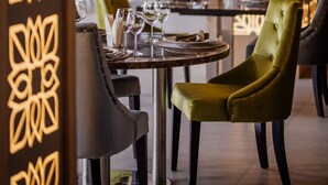 Uma área de refeições com uma mesa redonda, cadeiras e uma parede decorativa com padrões geométricos.