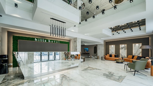 Um saguão de hotel moderno com balcão de recepção, área de estar e uma grande tela de televisão.