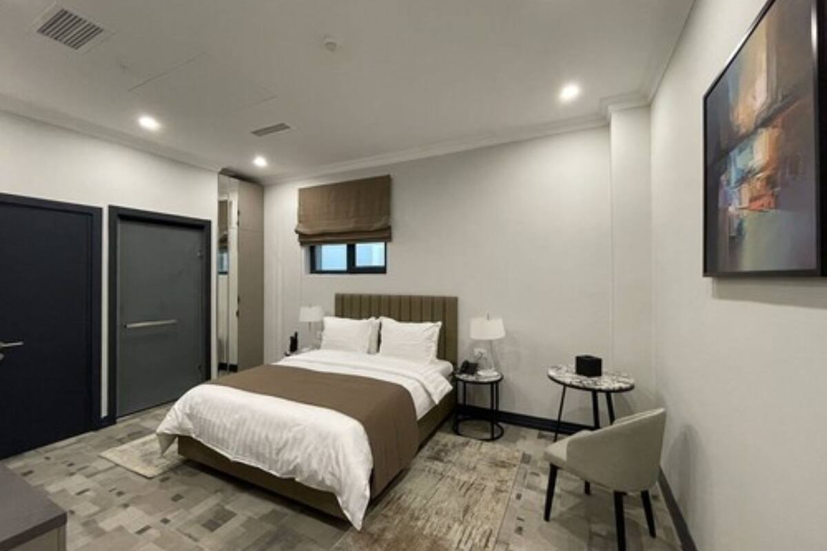 A modern hotel room with a large bed, bedside tables, a small round table, and a chair.