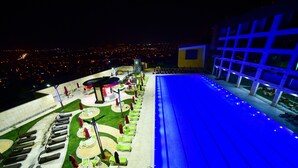 Terraço no telhado com espreguiçadeiras, guarda-sóis, piscina e vista para a cidade.