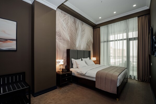 Habitación de hotel con una cama grande, una mesita de noche con lámpara, un banco y una pared con diseño de hojas.