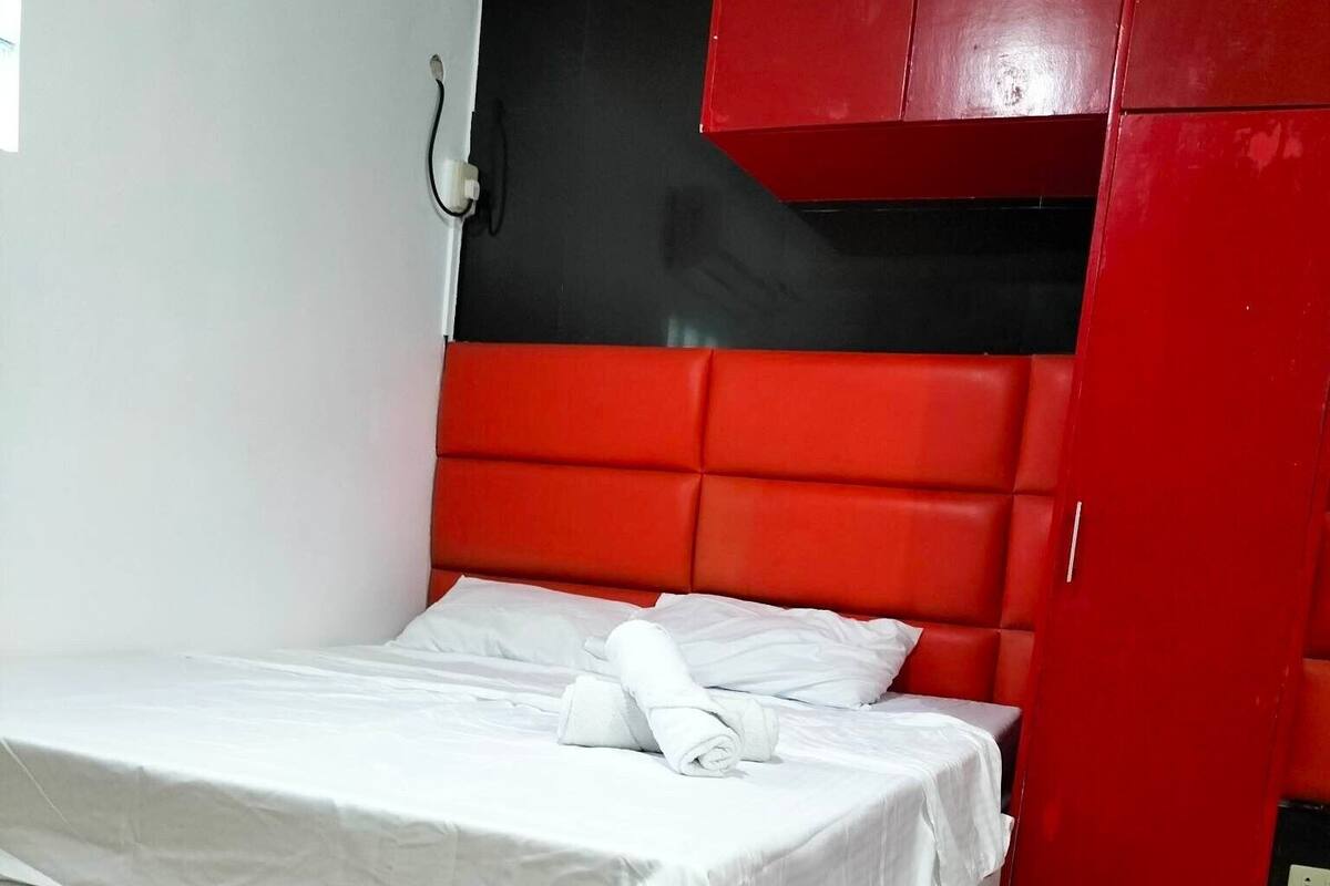 A single bed with white bedding in a room with a red wardrobe and a black headboard.