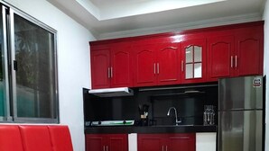A compact kitchen with red cabinets, a black countertop, and a stainless steel refrigerator. - Rapid Rise Hotel (Angeles City)