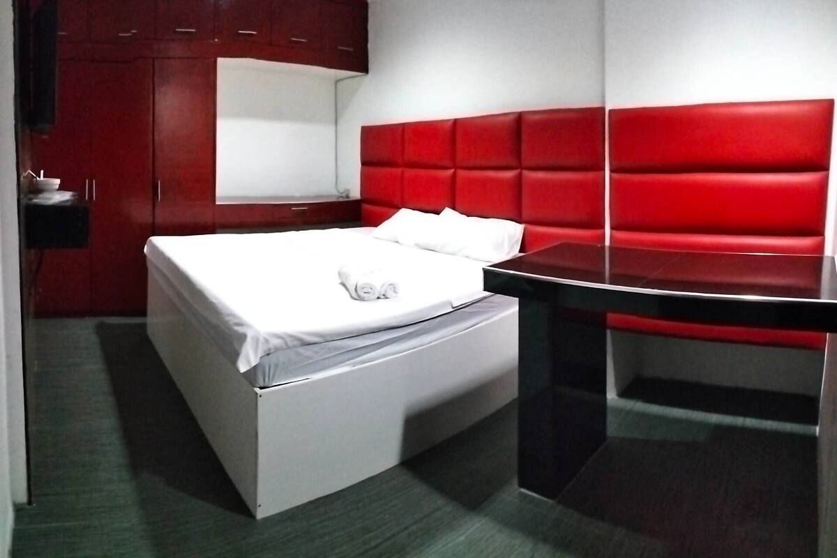 A modern room with a bed, a red upholstered headboard, a black table, and a small white bedside table.