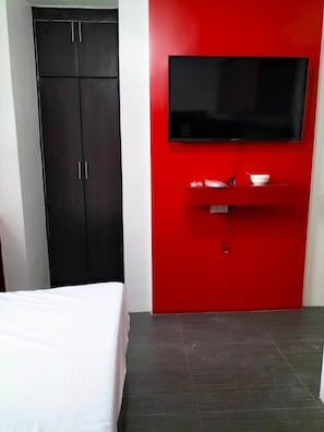 A bedroom with a bed, a wardrobe, a red wall-mounted TV, and a small shelf with a bowl and remote. - Rapid Rise Hotel (Angeles City)