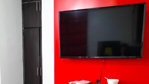 A room with a red accent wall, a flat-screen TV mounted above a red shelf, a dark wardrobe, and a marble-tiled table. - Rapid Rise Hotel (Angeles City)