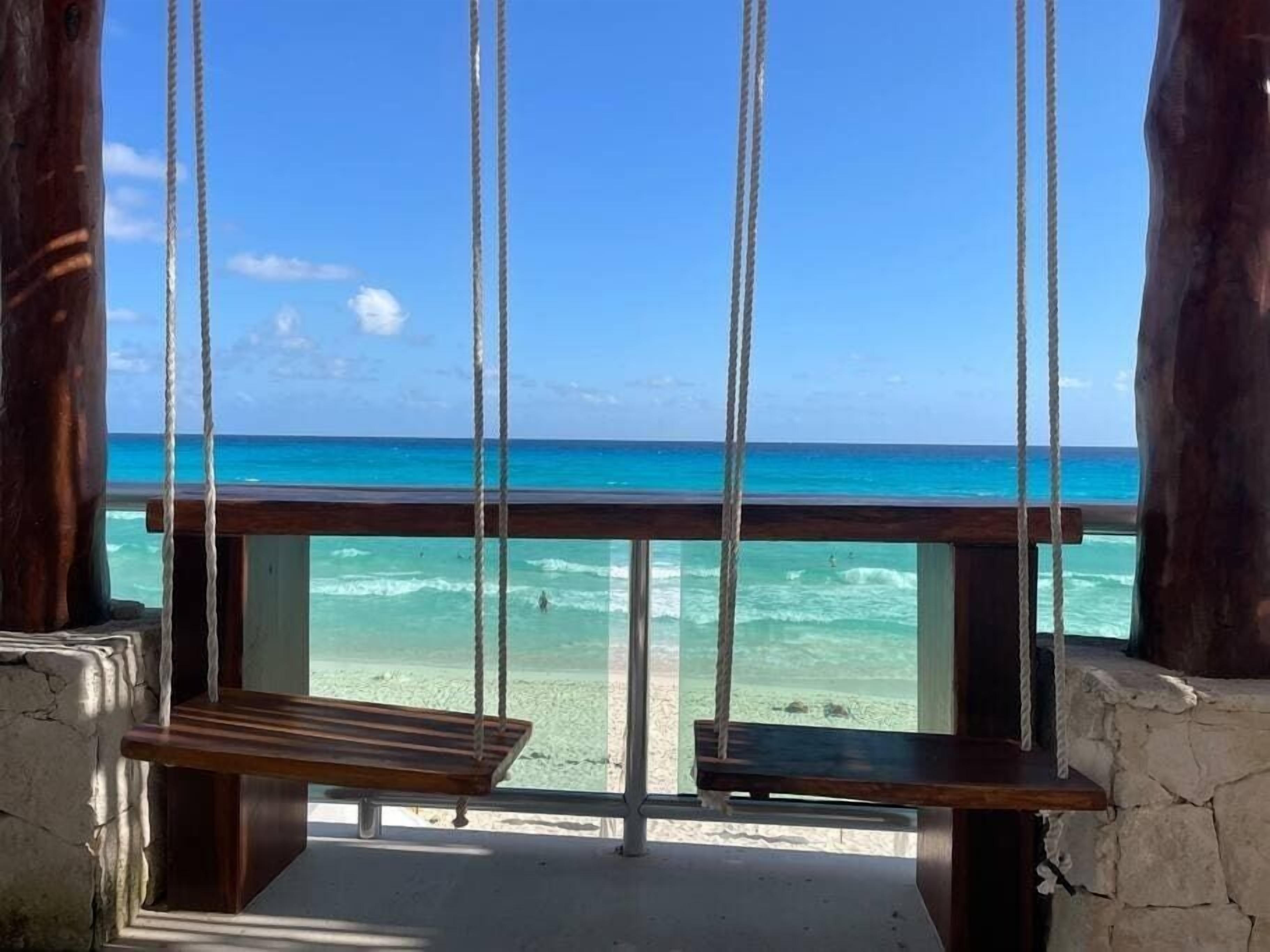 A wooden swing with ropes, overlooking a beach with turquoise water and clear skies.