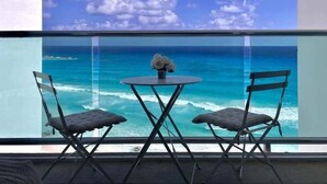 A balcony with two chairs and a small table, overlooking a clear blue sea and distant land. - Oceanview Studio, Beach Club & 2 Pools | Cancun (CancÃºn)