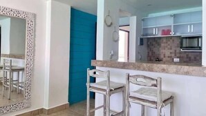 A modern kitchen with a blue accent wall, a large mirror, and a bar area with two stools. - Oceanview Studio, Beach Club & 2 Pools | Cancun (CancÃºn)