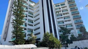 A multi-story hotel with balconies, a central vertical feature, and surrounding greenery. - Oceanview Studio, Beach Club & 2 Pools | Cancun (CancÃºn)