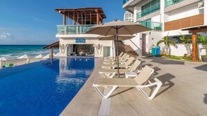 A hotel pool area with lounge chairs, a bar, and a view of the ocean. - Oceanview Studio, Beach Club & 2 Pools | Cancun (CancÃºn)