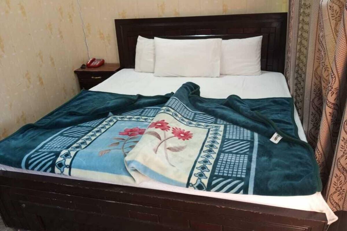 Una cama con cabecera oscura, almohadas blancas y colcha estampada de flores azules.