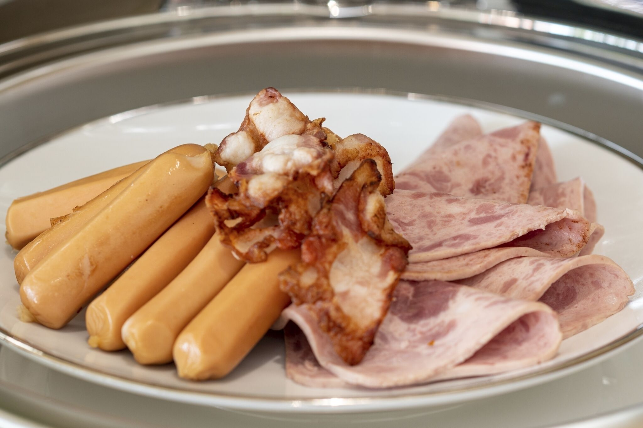 A plate with several hot dogs and slices of ham.