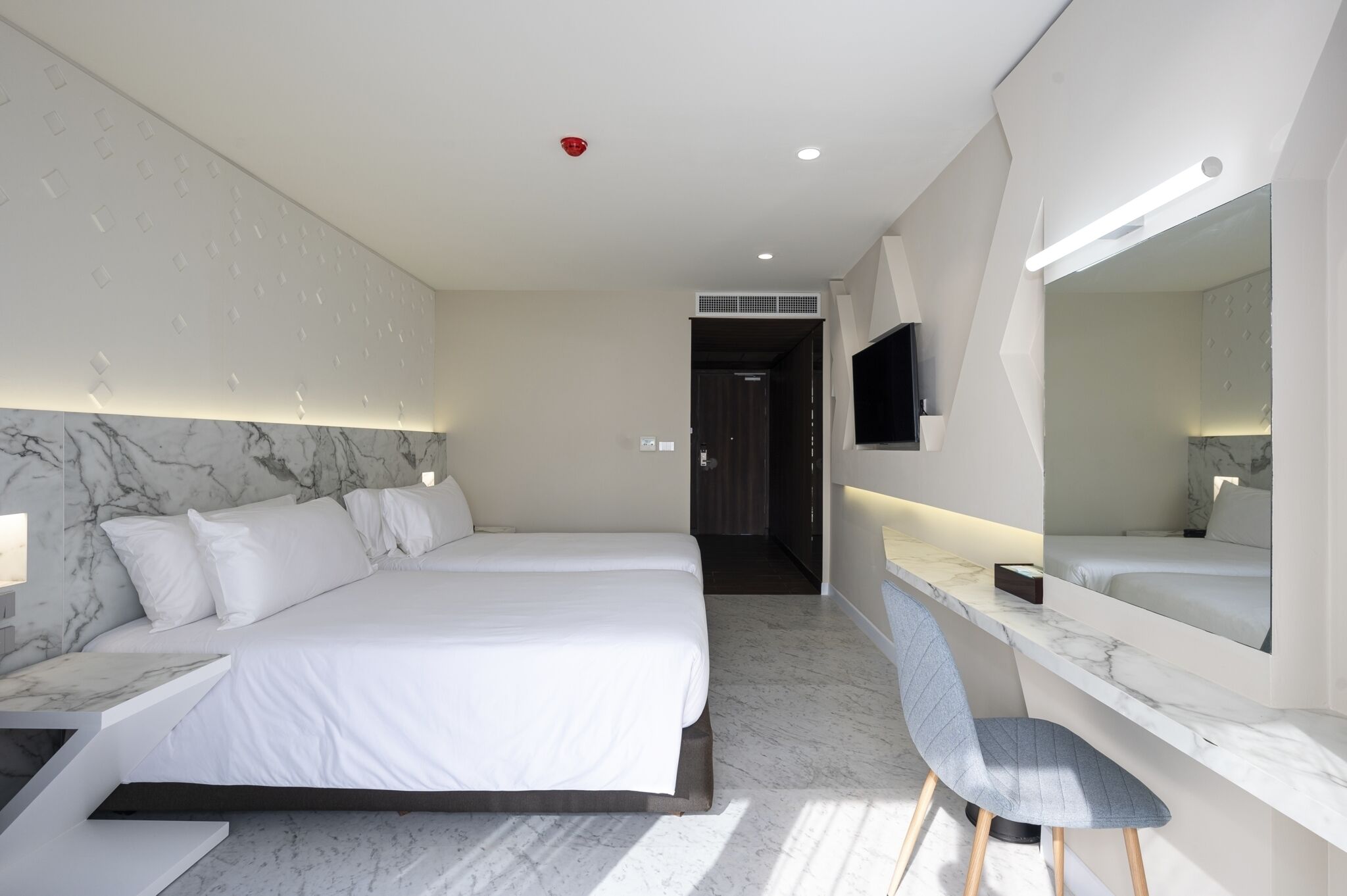 Een moderne hotelkamer met een groot bed, een bureau met stoel, een grote spiegel en een wand met een marmerlook.