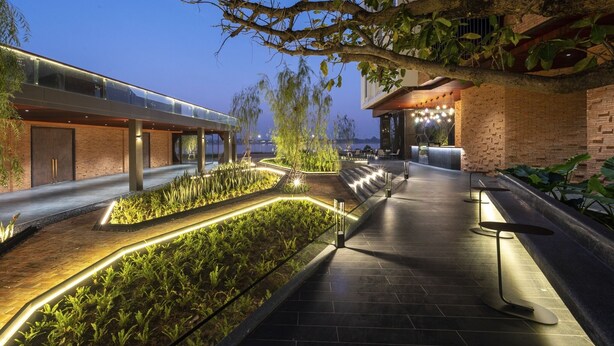 A modern outdoor area with a glass walkway, brick walls, and illuminated plants. - VELA Dhi Nakhon Phanom (Nakhon Phanom)