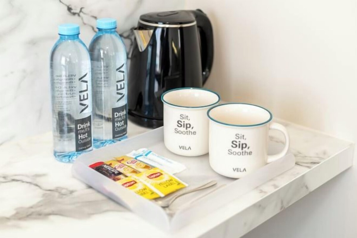 A marble countertop with a coffee maker, two water bottles, two mugs, and a tray with packets.